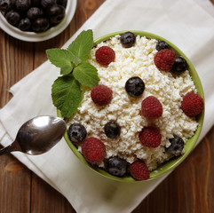 Cottage cheese with raspberries and blueberries in a bowl for healthy breakfast with ripe berries over rustic wooden background.
