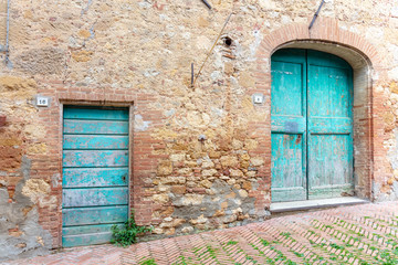 Fototapeta na wymiar Pienza, Tuscany. Two Old Green Weatherbeaten Wooden Front Doors on a slope