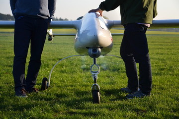 Man preparing unmanned aerial vehicle drone with light and camera for takeoff on ground, green...