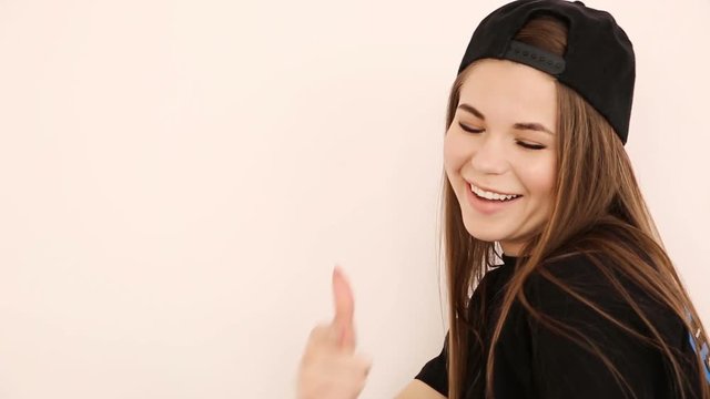 teenage girl in trendy hip hop clothes and cap posing against white wall