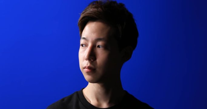 Portrait of Asian young man with dark and bright side of face turning his head on blue screen background