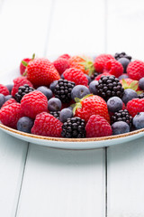 Fresh berry salad on blue dishes. Vintage wooden background.