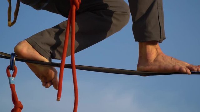 A barefooted man in sport pants walks along a tight rope against the blue sky