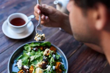 Rolgordijnen Man die heerlijke salade eet terwijl hij aan een bistrotafel zit © mavoimages
