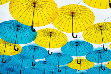 Fototapeta na wymiar Umbrellas float in sky on sunny day. Umbrella sky project installation. Outdoor art design and decor. Holiday and festival celebration. Shade and protection