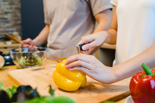 Woman hands cutting bell pepper in the kitchen. Beautiful happy asian couple are cooking in the kitchen. Young asian couple have romantic time while staying at home. Couple lifestyle at home concept.
