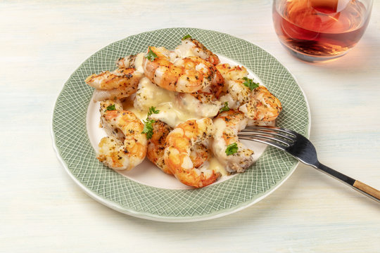 A photo of plate of cooked shrimps on a light background, with a glass of rose wine