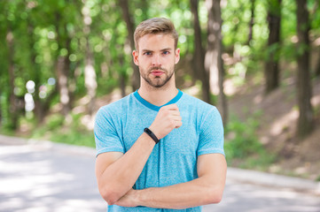 Man athlete on strict face posing with sportive equipment, nature background. Athlete with bristle with fitness tracker or pedometer. Sport gadget concept. Sportsman training with pedometer gadget