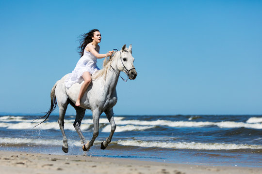 Girl storming through the beach on a white horse