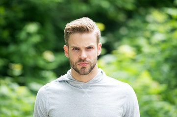 Naklejka na ściany i meble Guy bearded and attractive cares about appearance. Man with bristle on serious face, green nature background, defocused. Metrosexual concept. Man with beard or unshaven guy looks handsome and cool