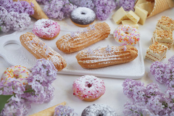 Eclairs and donuts with coffee with lilac flowers, on a marble background, Light background, Confectionery in a blogger style