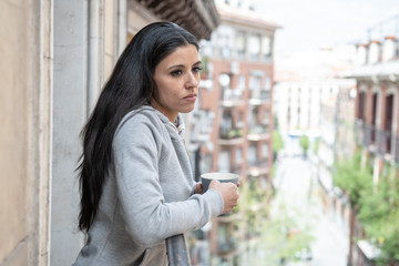 Fototapeta premium Young attractive sad woman suffering from depression drinking a cup of coffee on a balcony at home