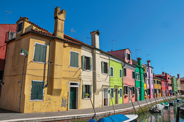 Fototapeta na wymiar Panoramic view of colorful buildings, people and boats in front of a canal at Burano, a gracious little town full of canals, near Venice. Located in the Veneto region, northern Italy