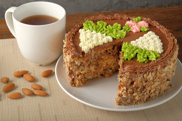 Cut homemade Kiev cake, cup of tea and scattered almonds on textile napkin on the wooden table. The known ukrainian delicacy. Close-up view.