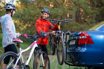 Fototapeta na wymiar Young Couple Unmounting Mountain Bikes from Bike Rack on the Car. Adventure and Family Travel Concept.