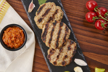 Grilled Veal minced meat with spices on black stone and wooden background 