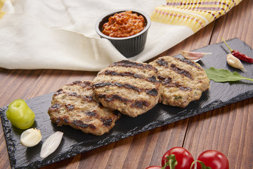 Grilled Veal minced meat with spices on black stone and wooden background 