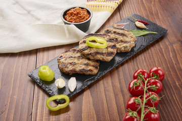 Grilled Veal minced meat with spices on black stone and wooden background 
