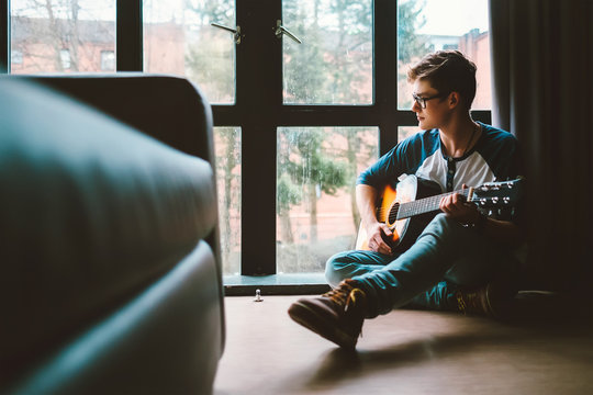 Guy plaing on guitar sits on the floor at home