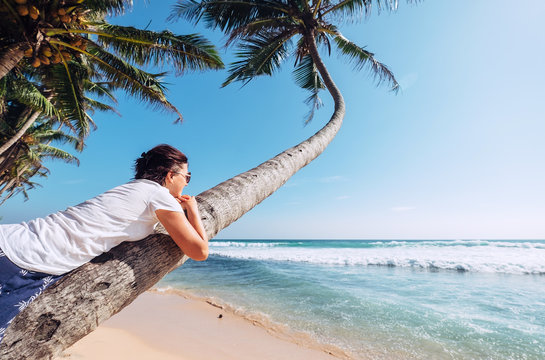 Woman lies on the palm tree and looks on ocaen waves. Summer vacation concept image