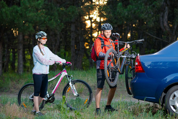 Young Couple Unmounting Mountain Bikes from Bike Rack on the Car. Adventure and Family Travel Concept.
