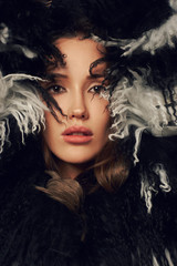 Portrait of young beautiful brunette woman wearing elegant faux fur coat with long black and white hair. Gorgeous sexy caucasian female model with evening makeup posing with raised crossed arms.