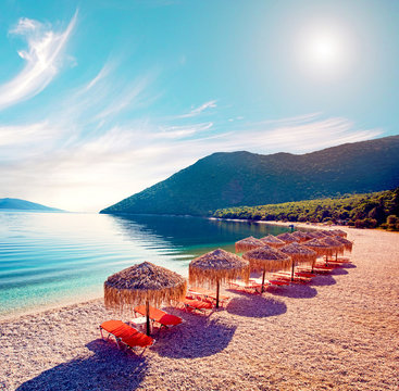 Fabulous beautiful magic landscape with umbrellas and orange sun beds on the seafront on Antisamos Beach on a sunny day on the coast of the Ionian Sea in Kefalonia, Greece. Amazing places. 