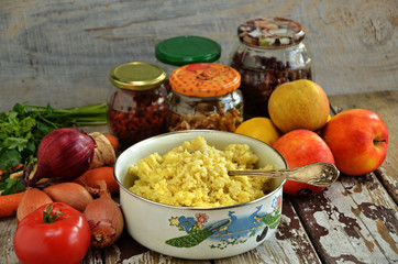 Cooked millet in a pot. Fruits and vegetables on a wooden background