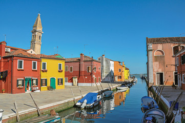 Fototapeta na wymiar Overview of colorful buildings, bell tower and boats in blue sunny day, facing a canal at Burano, a gracious little town full of canals, near Venice. Located in the Veneto region, northern Italy