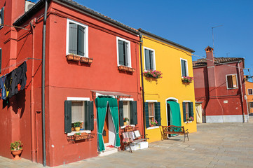 Overview of colorful buildings and clothes hanging in a blue sunny day, in front of a canal at Burano, a gracious little town full of canals, near Venice. Located in the Veneto region, northern Italy