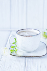 White cup of coffee cappuccino and white freesia flower on white wooden background. Free space, vertical photo