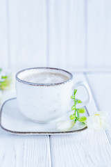 White cup of coffee cappuccino and white freesia flower on white wooden background. Free space, vertical photo