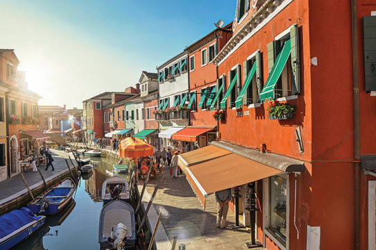 View of colorful buildings, people and boats in front of a canal at Burano, a gracious town full of canals, near Venice. Veneto region, northern Italy. Retouched photo