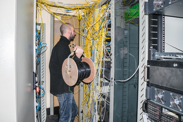 Man with a hub of utp cable works in the server room of the data center. The technician is near the...