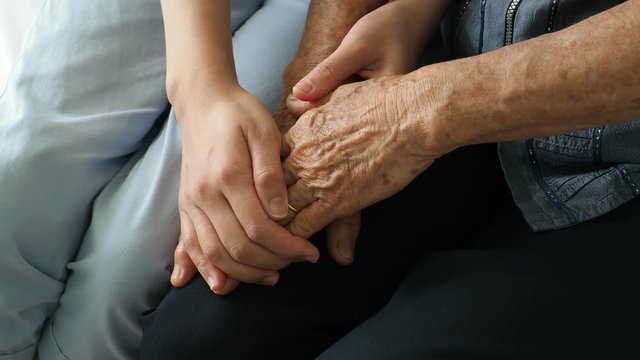 Young woman's hands comforting an elderly pair of hands.