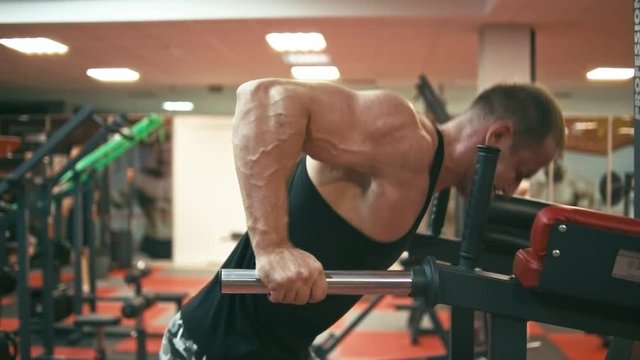 Bodybuilder in gym doing upright dip, shallow depth of field. Slow motion