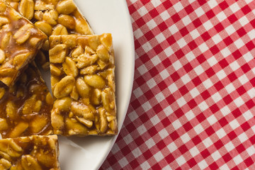 Candy with peanut: Pe de Moleque in Brazil and Chikki in India. Sweet food of Festa Junina, a typical brazilian party. Snack on plate, red plaid table.
