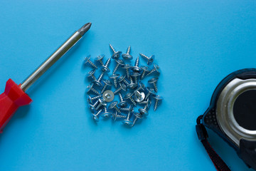 Red screwdriver, a bunch of nails, a tape measure on a blue background