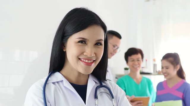 Beautiful asian doctor standing and smiling in front of medical team meeting on background
