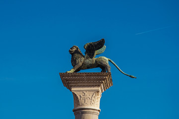 Close-up of column with the winged lion, symbol of Venice, and blue sunny sky in Piazza San Marco. At the city of Venice, the historic and amazing marine city. Located in Veneto region, northern Italy