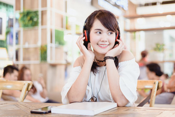 Portrait of beautiful Asian young woman smile and listening music with headphone at the coffee shop.Happiness and relaxing in workout time concept.
