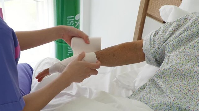 Nurse at the hospital bandaging the hand with a medical bandage for broken arm of senior patient 