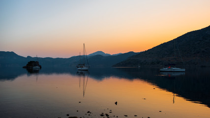 Fototapeta premium A calm sea at sunrise. Reflection of boats and hills in the water. Summer background