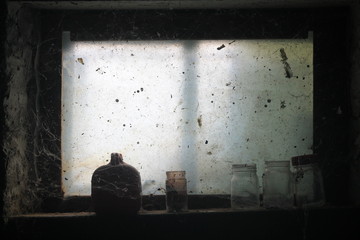 Interior view of frosty window in derelict building. Glass bottles on windowsill among cobwebs in dark room