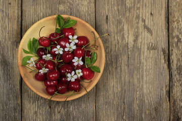 red cherries in wooden plate on wooden background