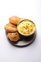 Shrikhand with fried Puri / Poori served in a bowl and plate over moody background. Selective focus