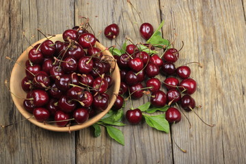 red cherries with leaves in wooden plate on wooden background