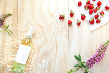 Obraz na płótnie Canvas A bottle of white wine on a wooden background with strawberries and flowers