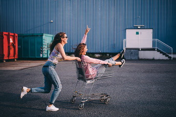 Young adult hipster friends having fun with shopping trolley
