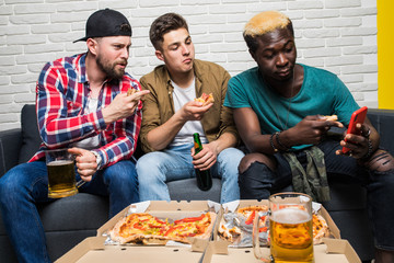 Fototapeta na wymiar Attractive three man with stubble show photo on smart phone to his excited surprised friends, together sitting in living room having pizza, glasses, pints with beer chips in hands speaking, talking